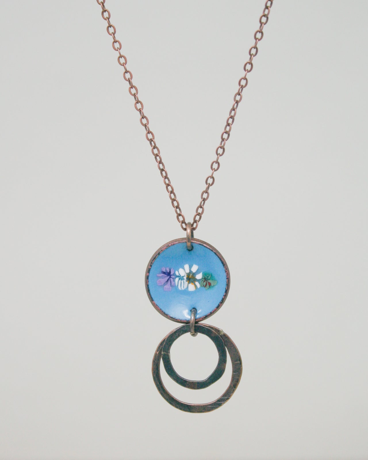 A necklace with a blue circular pendant featuring a floral design, hanging from a chain.