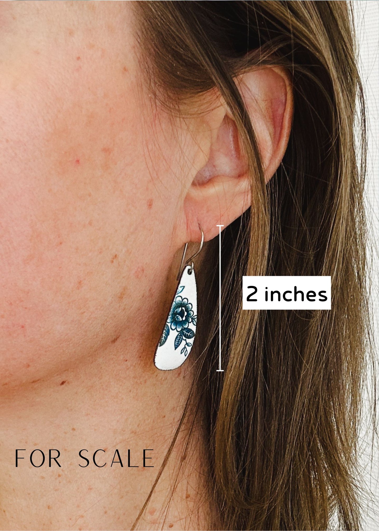 A close-up of a person's ear with a floral earring, and a scale indicating the earring is 2 inches in length.