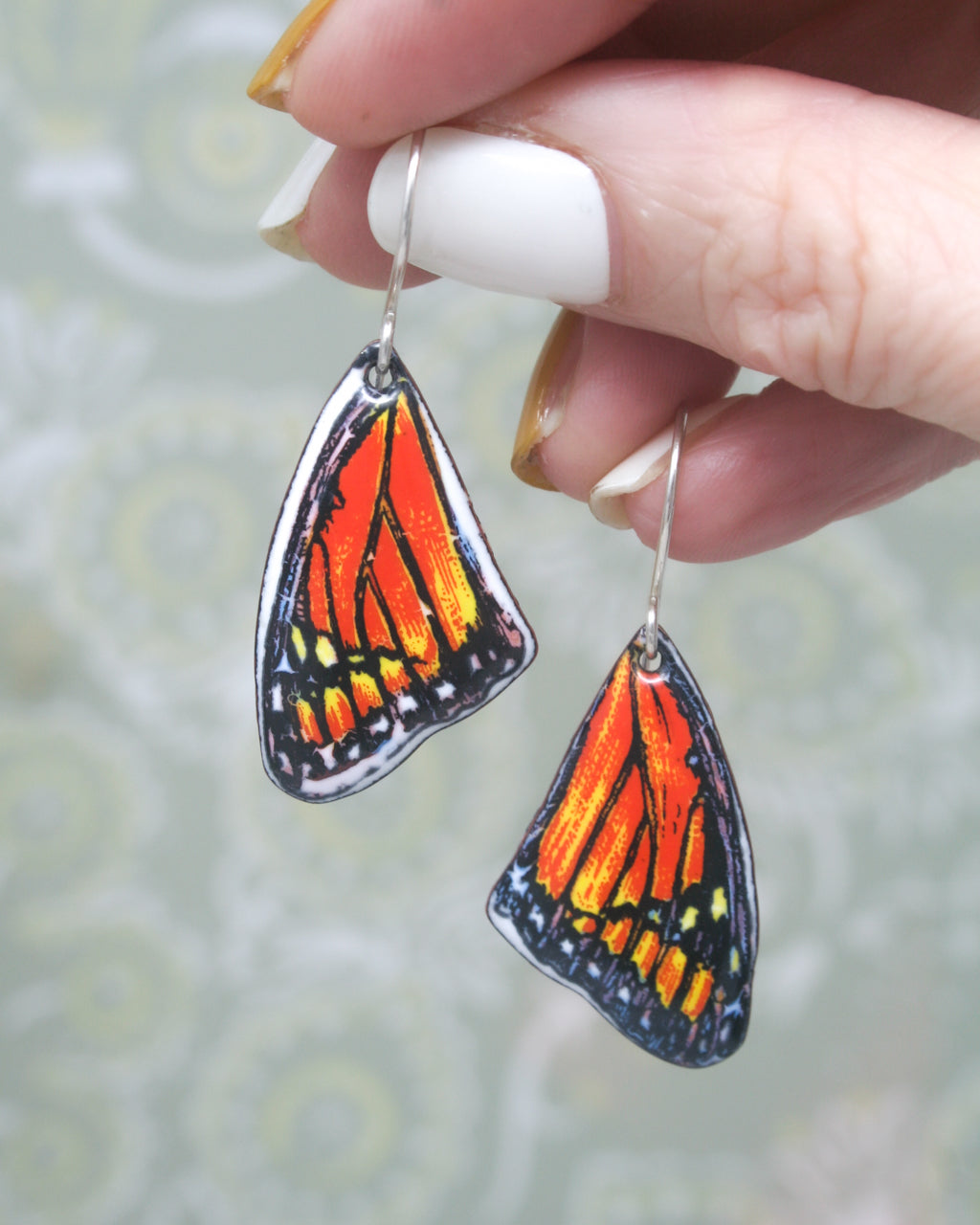 a woman's hand holding a pair of orange and black earrings