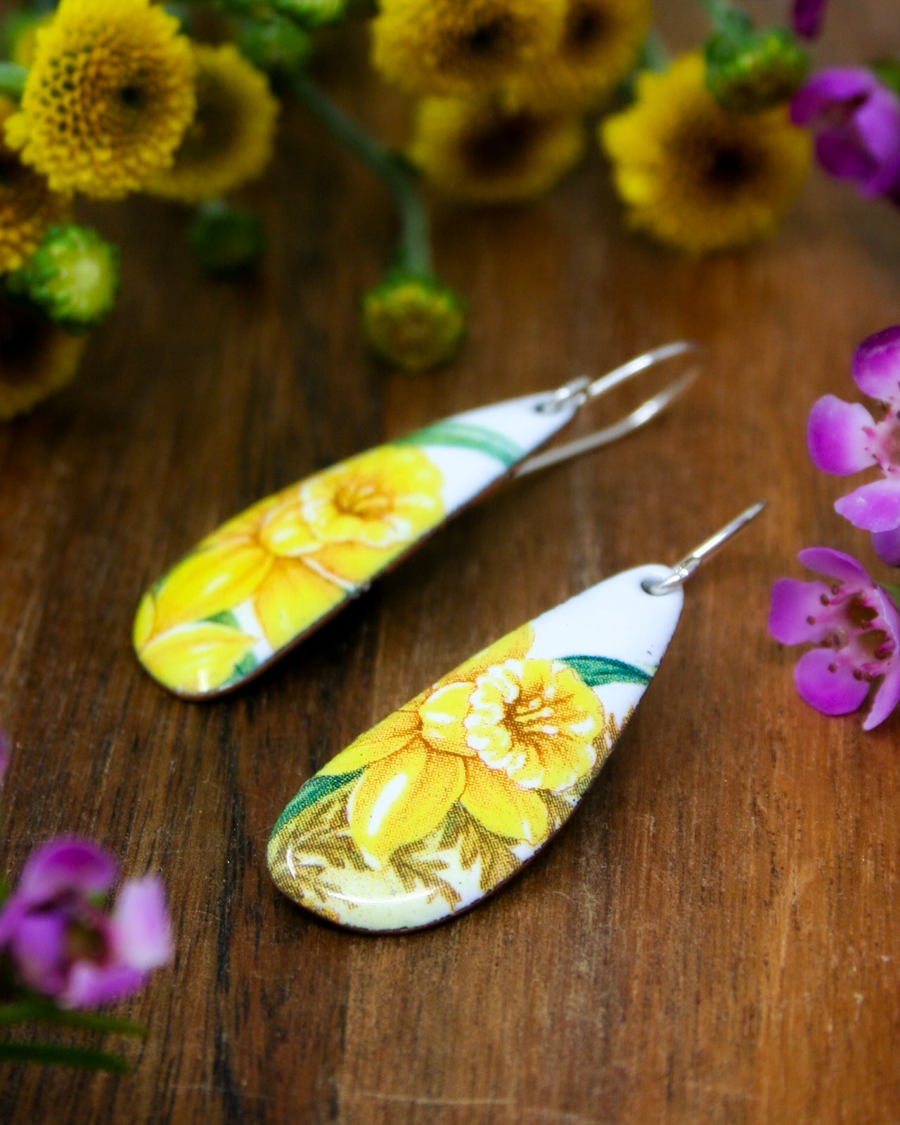 a pair of yellow and white earrings with flowers in the background