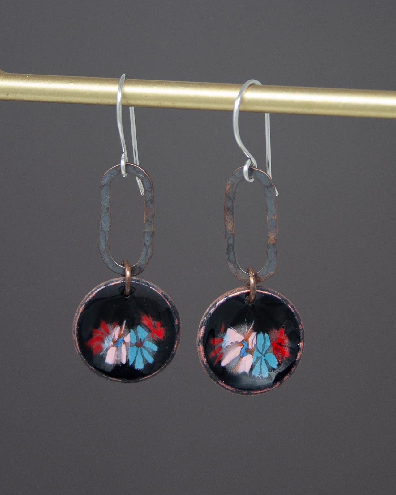 A pair of earrings with a floral design on the circular pendants, hanging from a gold-colored metal hook.