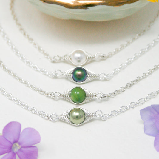 A collection of silver necklaces with various colored beads, including green, white, and purple, arranged in a row on a white background.