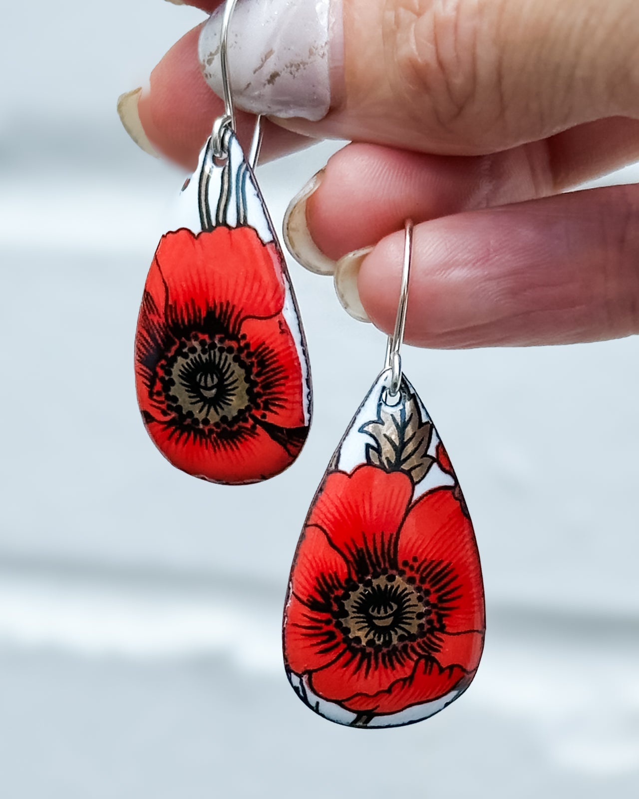 A hand holding a pair of red and white earrings with a floral design.