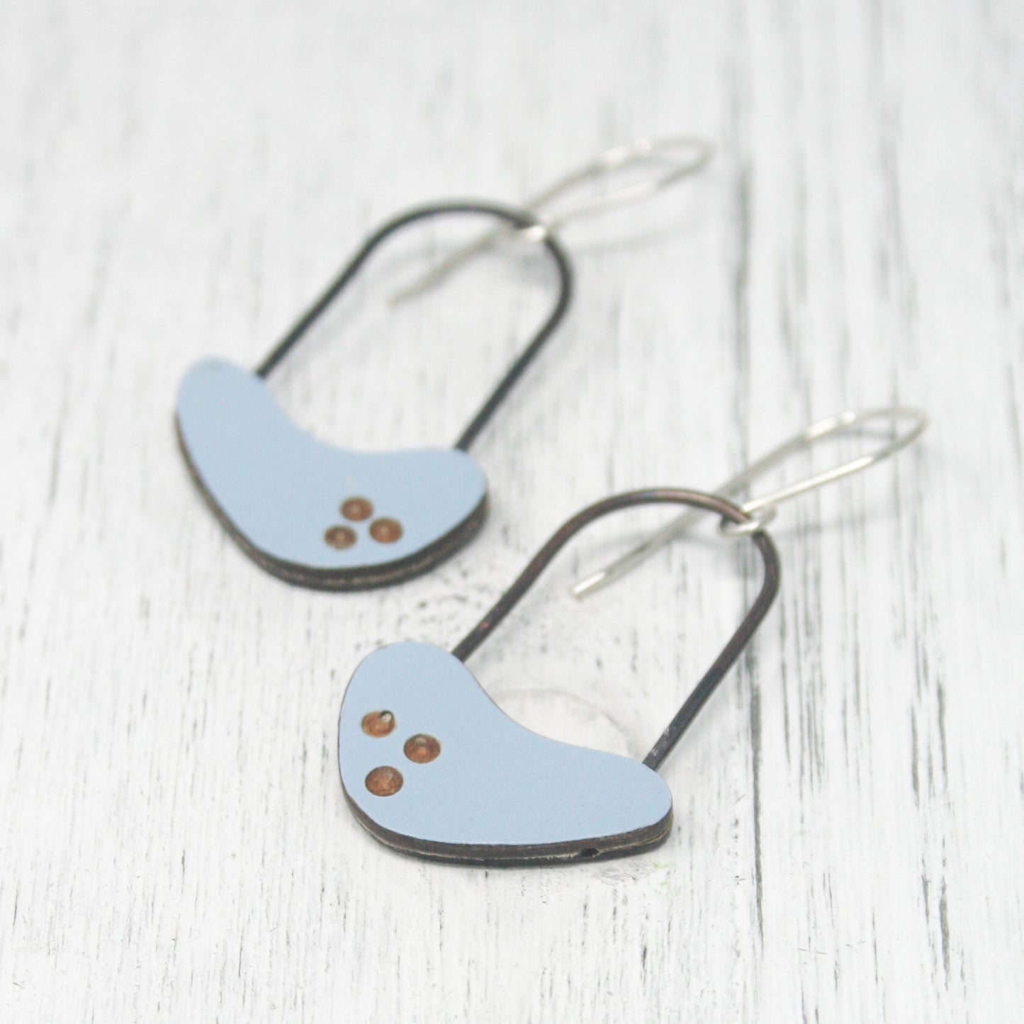 A pair of blue earrings with small brown dots on the surface, resting on a white wooden surface.