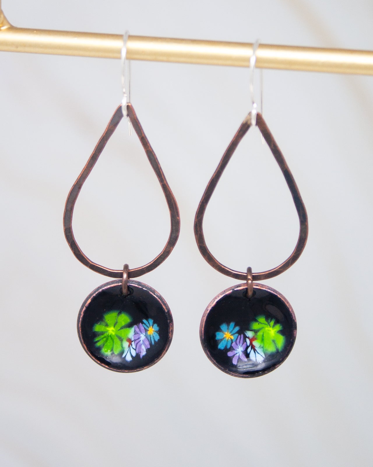A pair of earrings with a floral design on the center, featuring green and purple flowers.