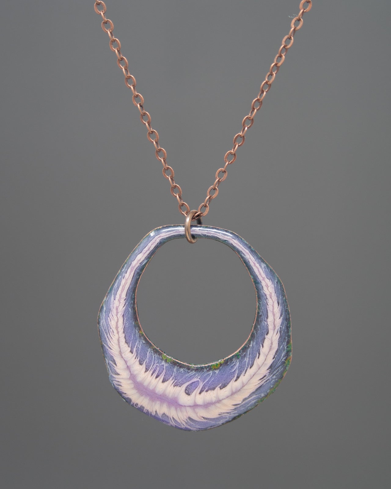 A necklace with a circular pendant featuring a design of purple and white feathers.
