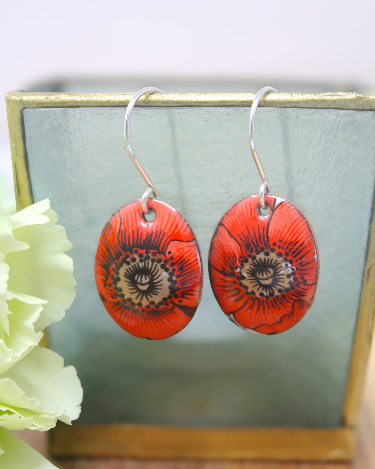 A pair of red earrings with a floral design, displayed on a stand with a green background.