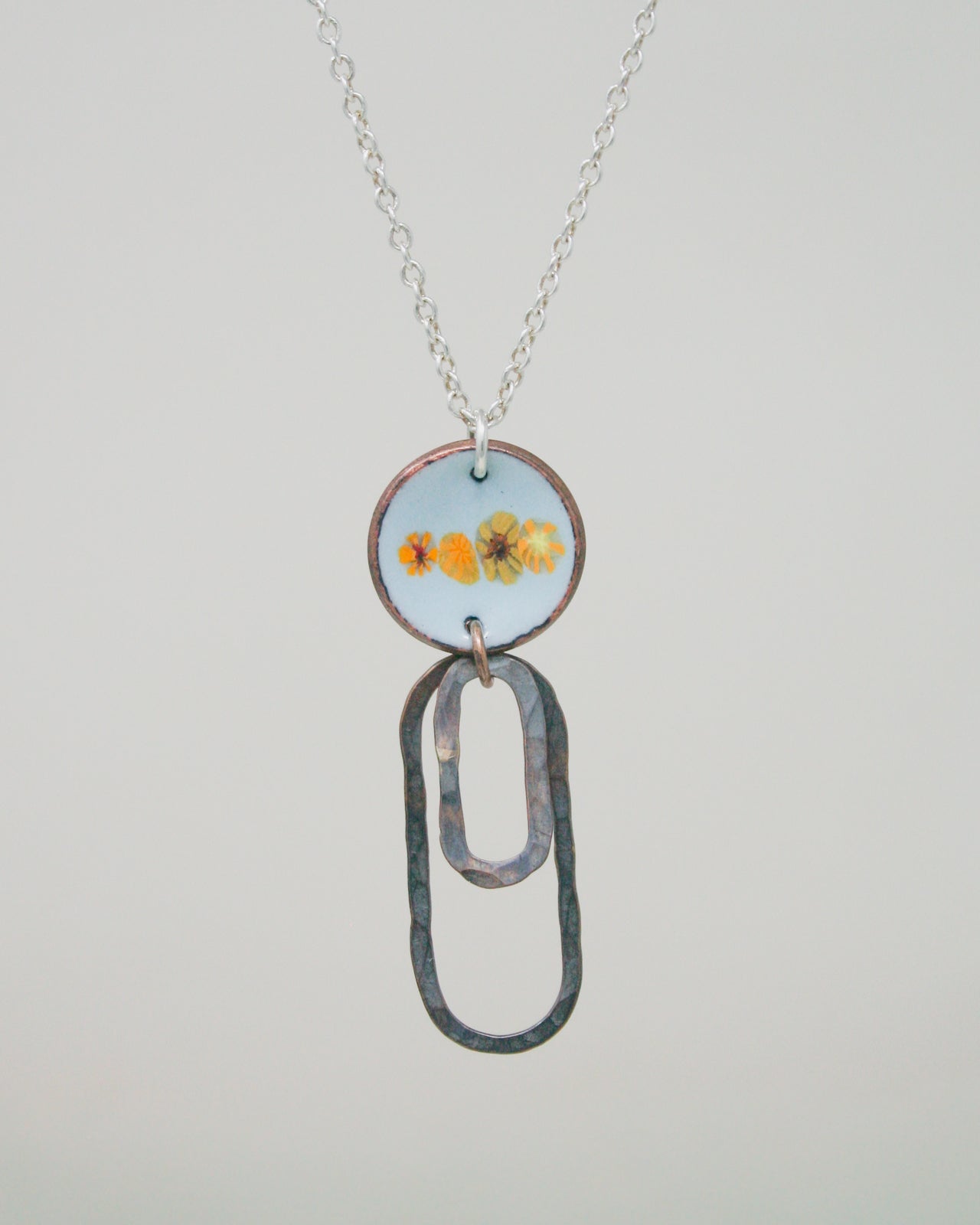 A necklace with a pendant featuring a circular design with three orange flowers on it, hanging from a chain.