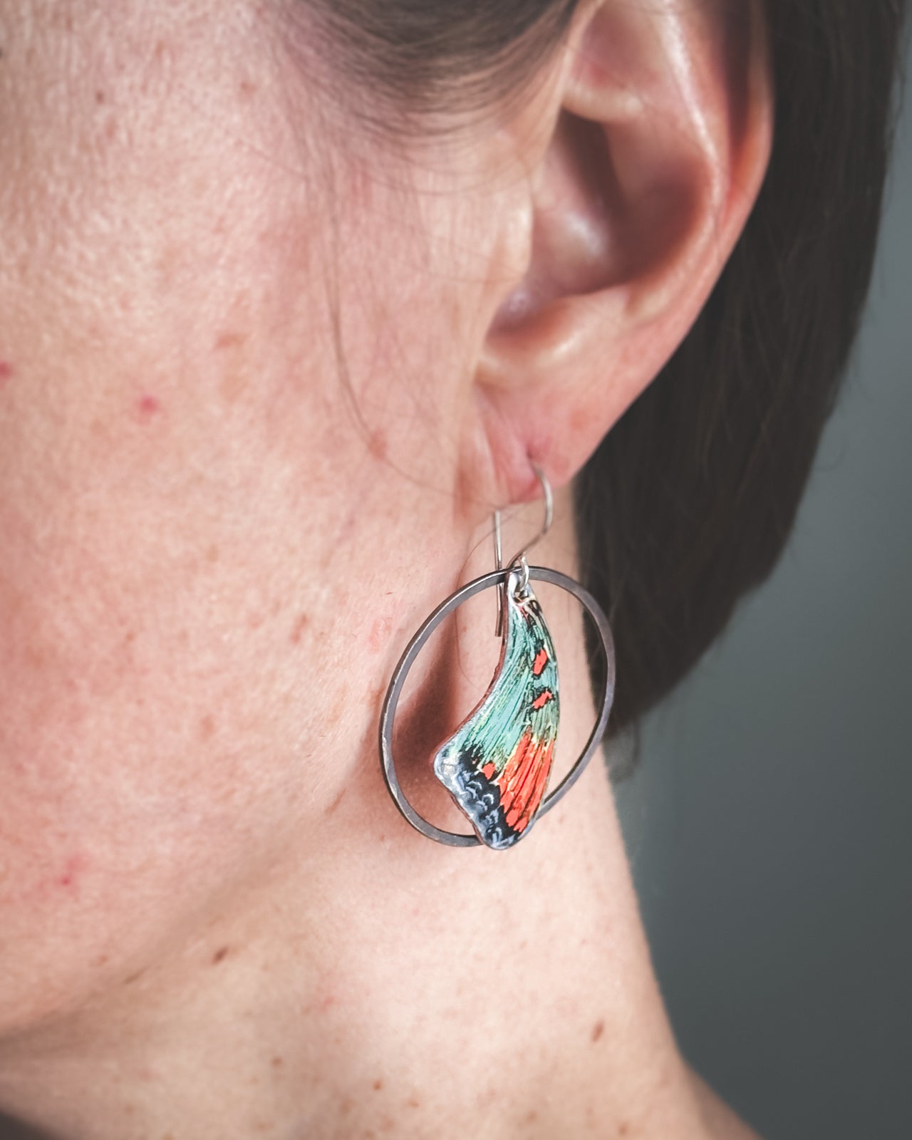 A close-up view of a person's ear wearing a pair of colorful earrings with a butterfly design.