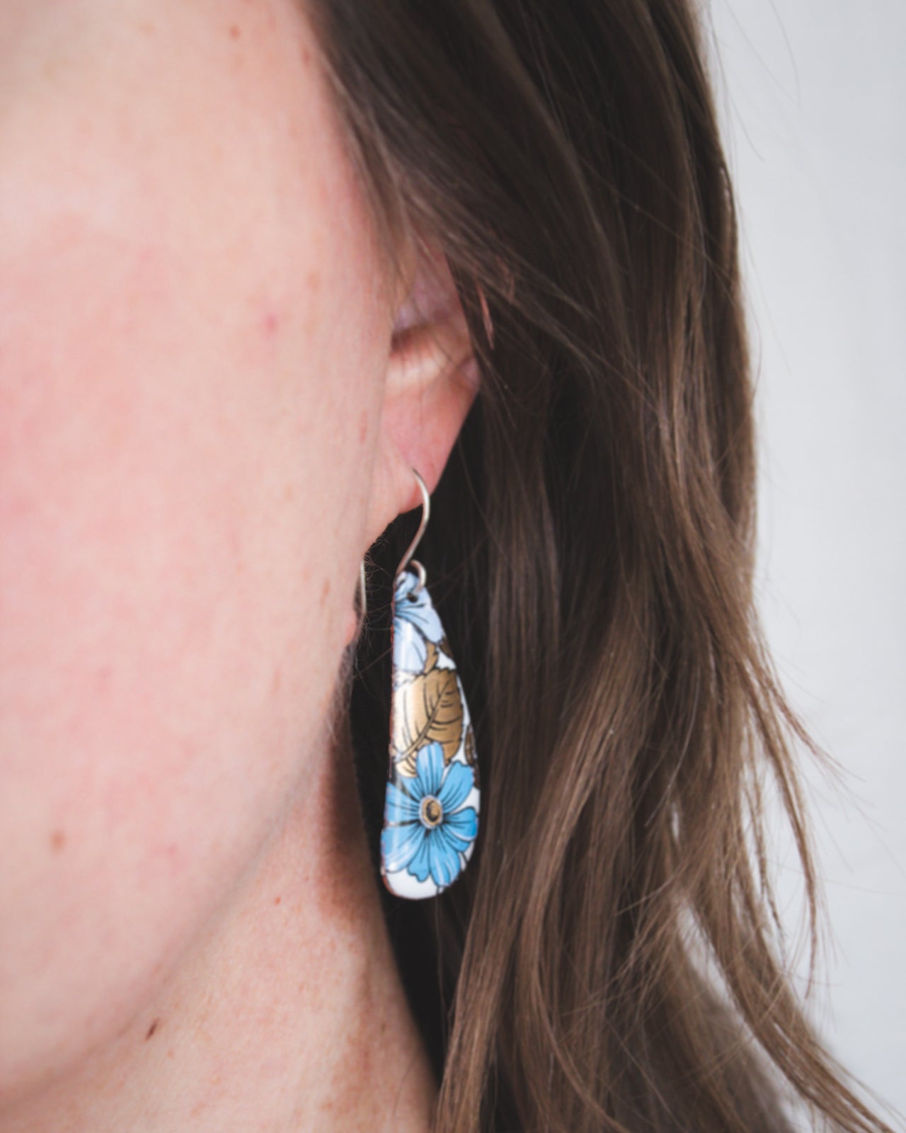 A close-up view of a person's ear wearing a pair of earrings with a floral design.