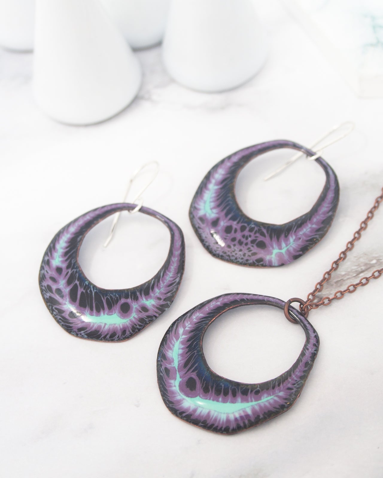 a pair of purple and blue earrings and a necklace with a chain, all displayed on a white surface.