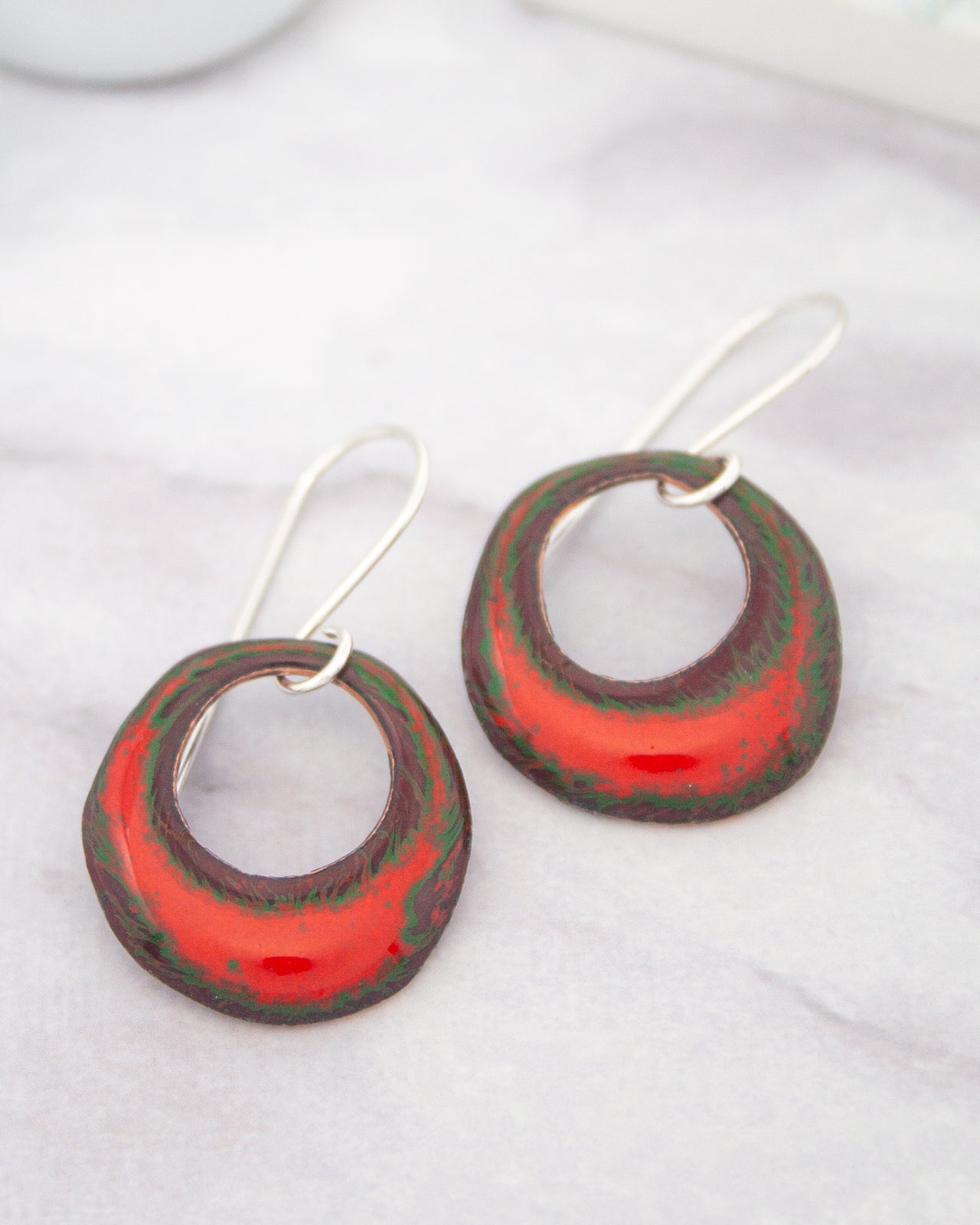 A pair of red and green earrings with circular designs, resting on a white surface.