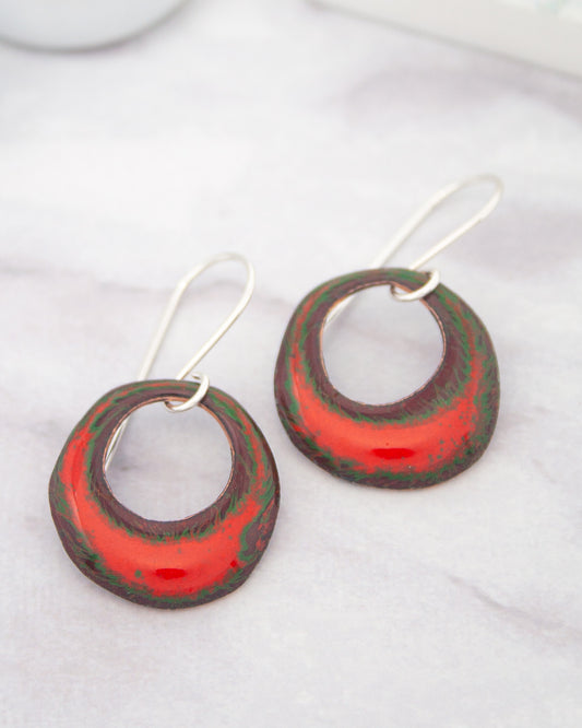 A pair of red and green earrings with circular designs, resting on a white surface.