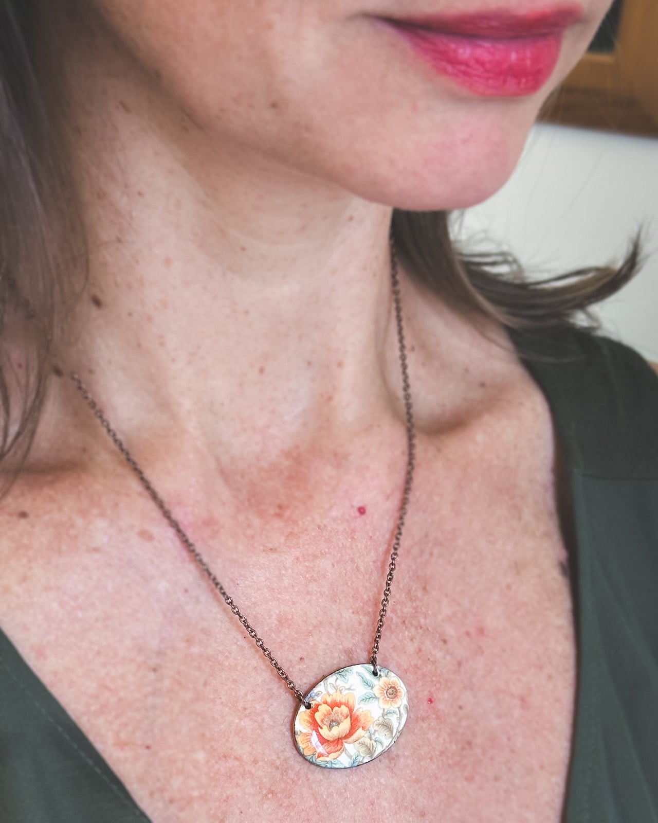 A woman wearing a necklace with a floral pendant is shown in the image.