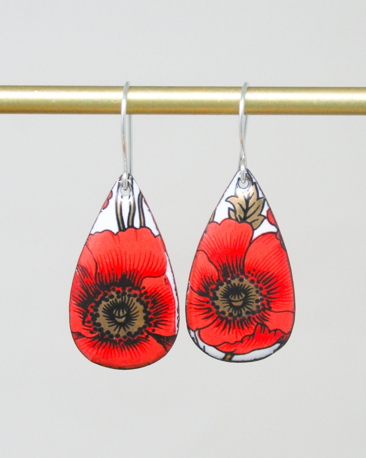 A pair of red earrings with a floral design hanging from a gold bar.