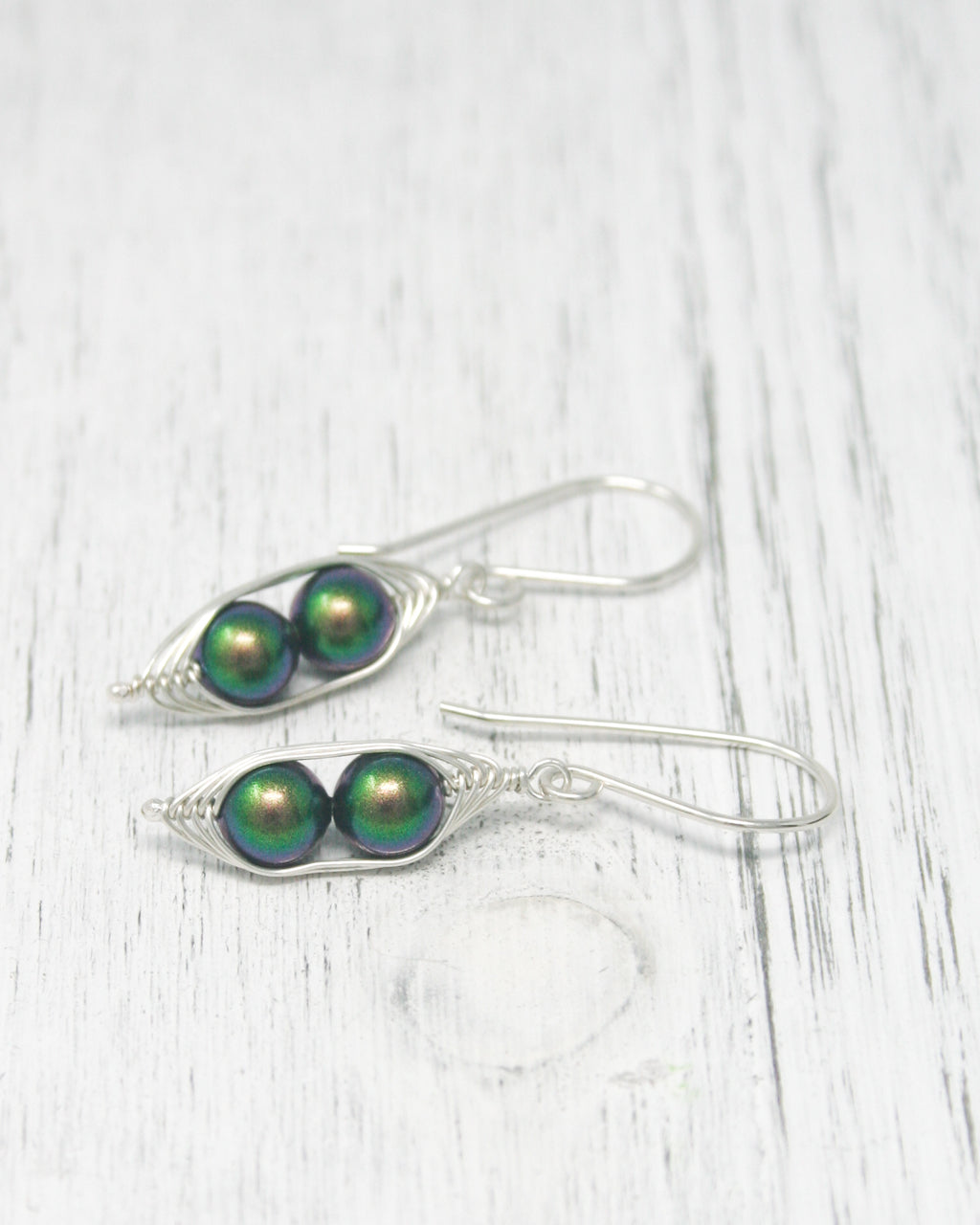 a pair of silver and green earrings on a white table