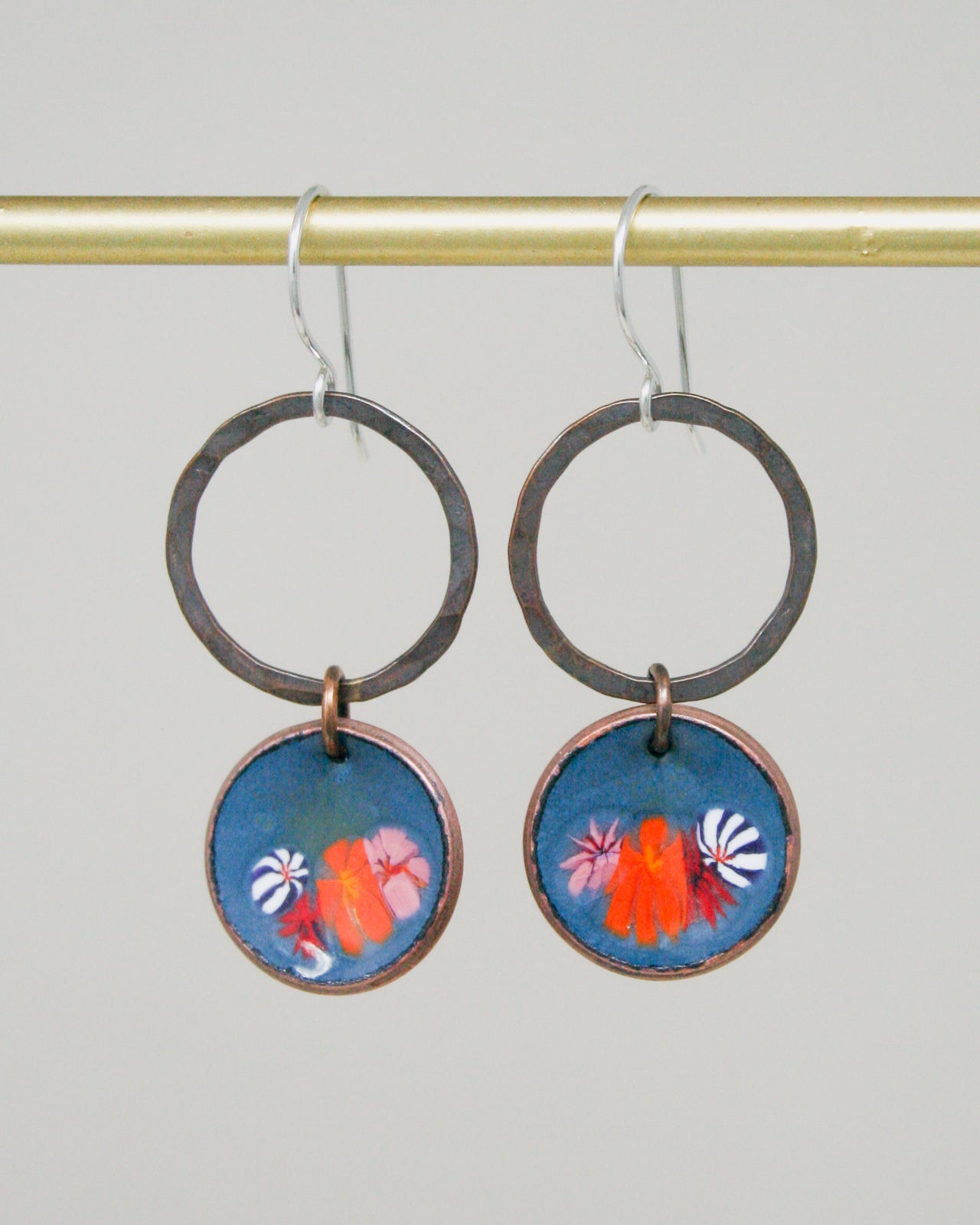 A pair of earrings with a blue circular design featuring a floral pattern and two orange flowers.