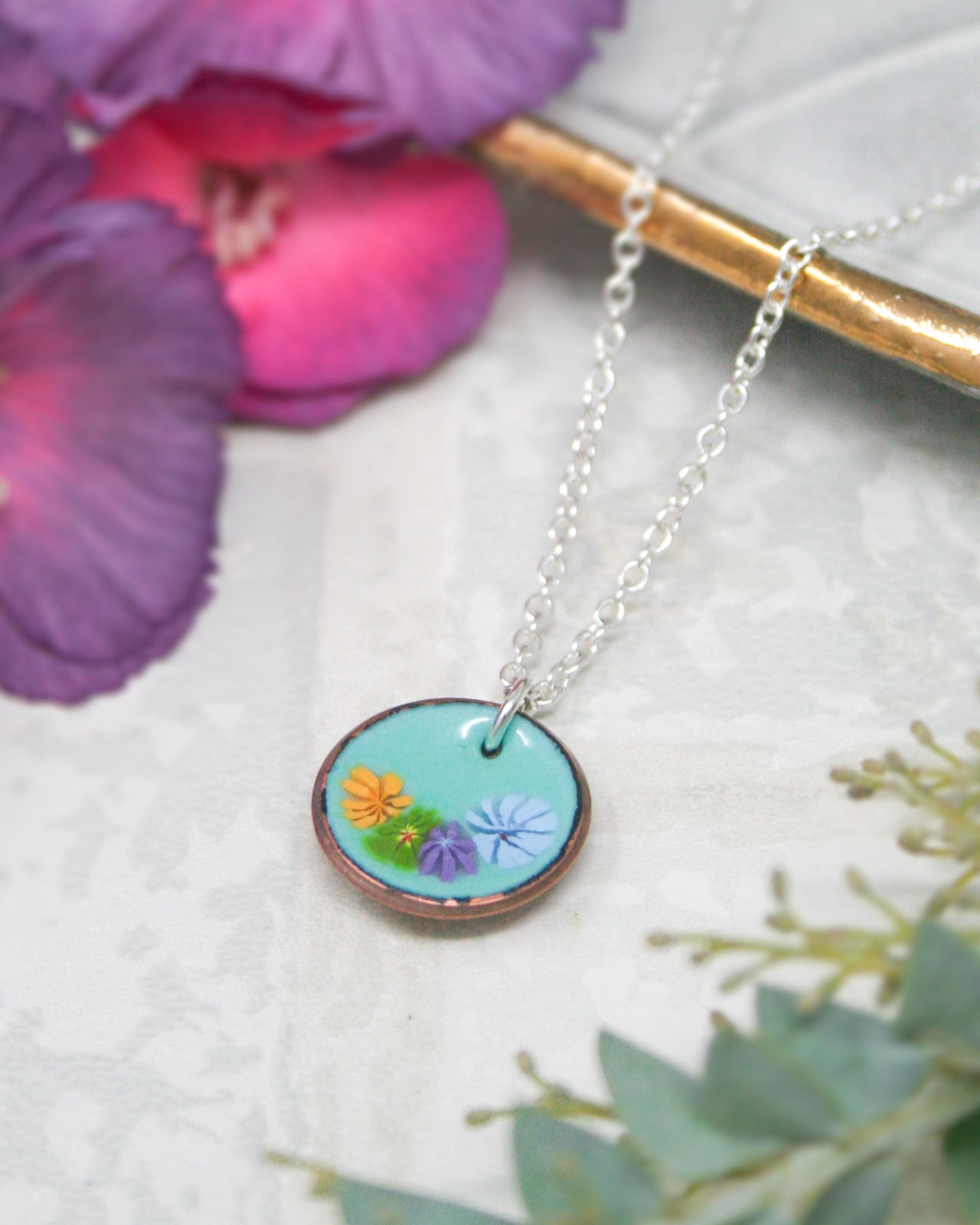 A necklace with a circular pendant featuring a floral design in blue, green, and orange colors.