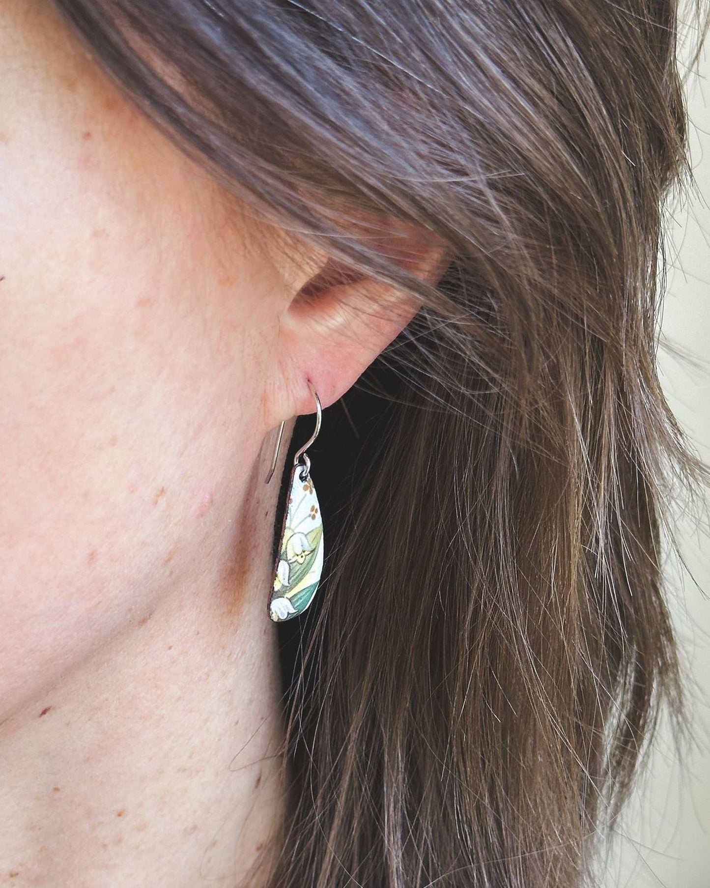 A close-up view of a person's ear with a floral earring hanging from it.