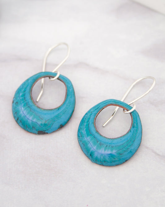 A pair of turquoise earrings with a floral design, resting on a white surface.