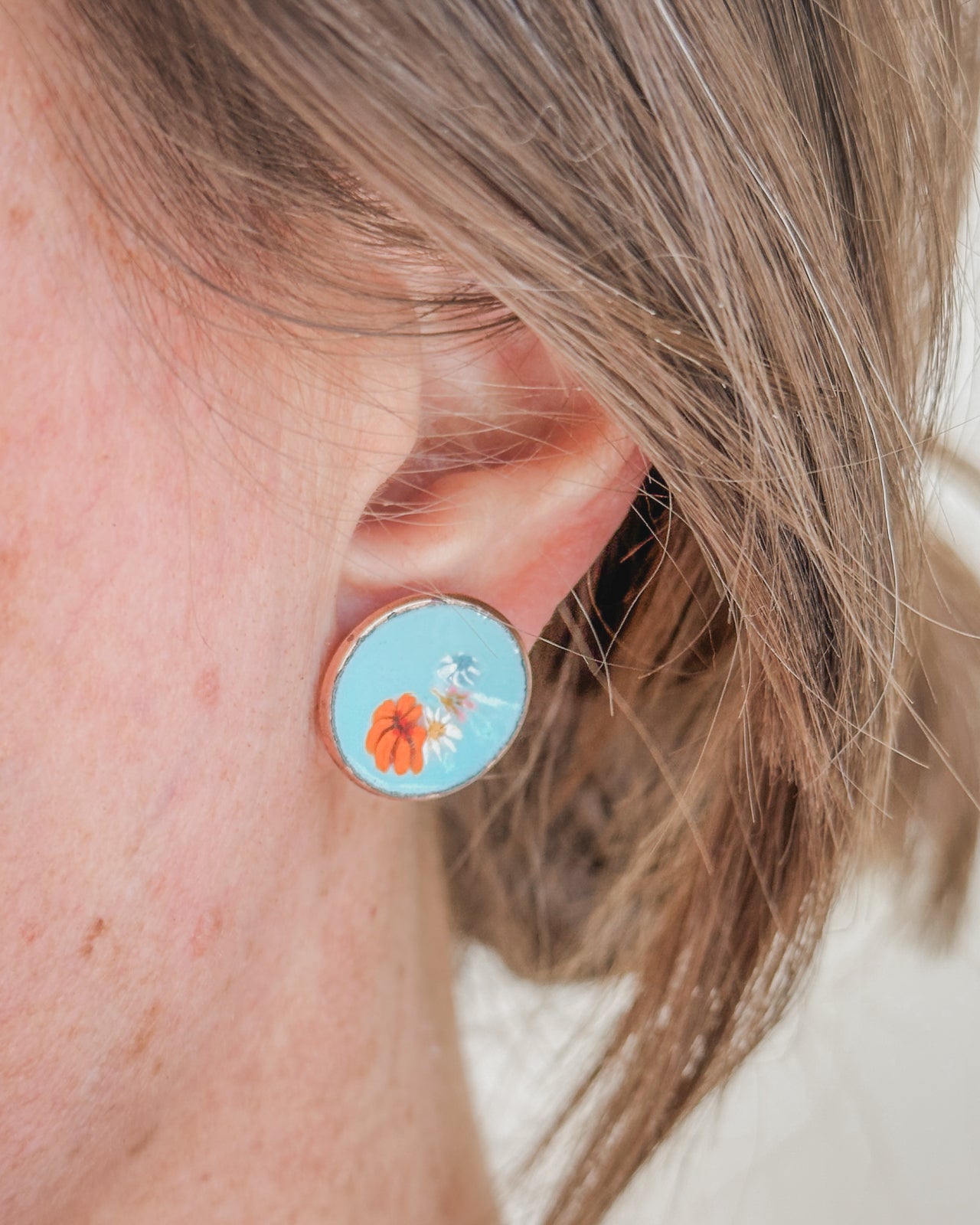 A close-up of a person's ear wearing a blue and orange earring with a floral design.