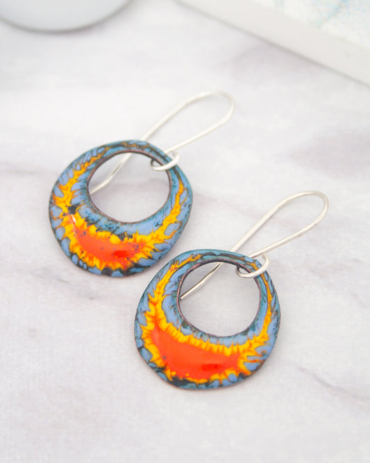 a pair of colorful earrings with blue and orange designs, resting on a white surface.