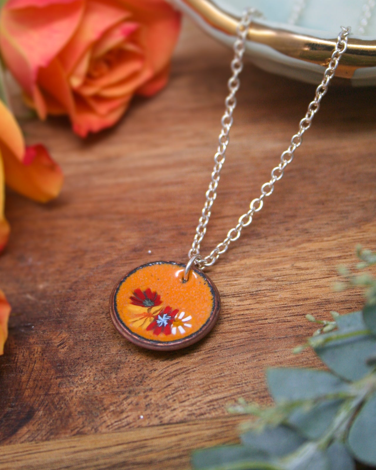 a necklace with a circular pendant adorned with a floral design, resting on a wooden surface.