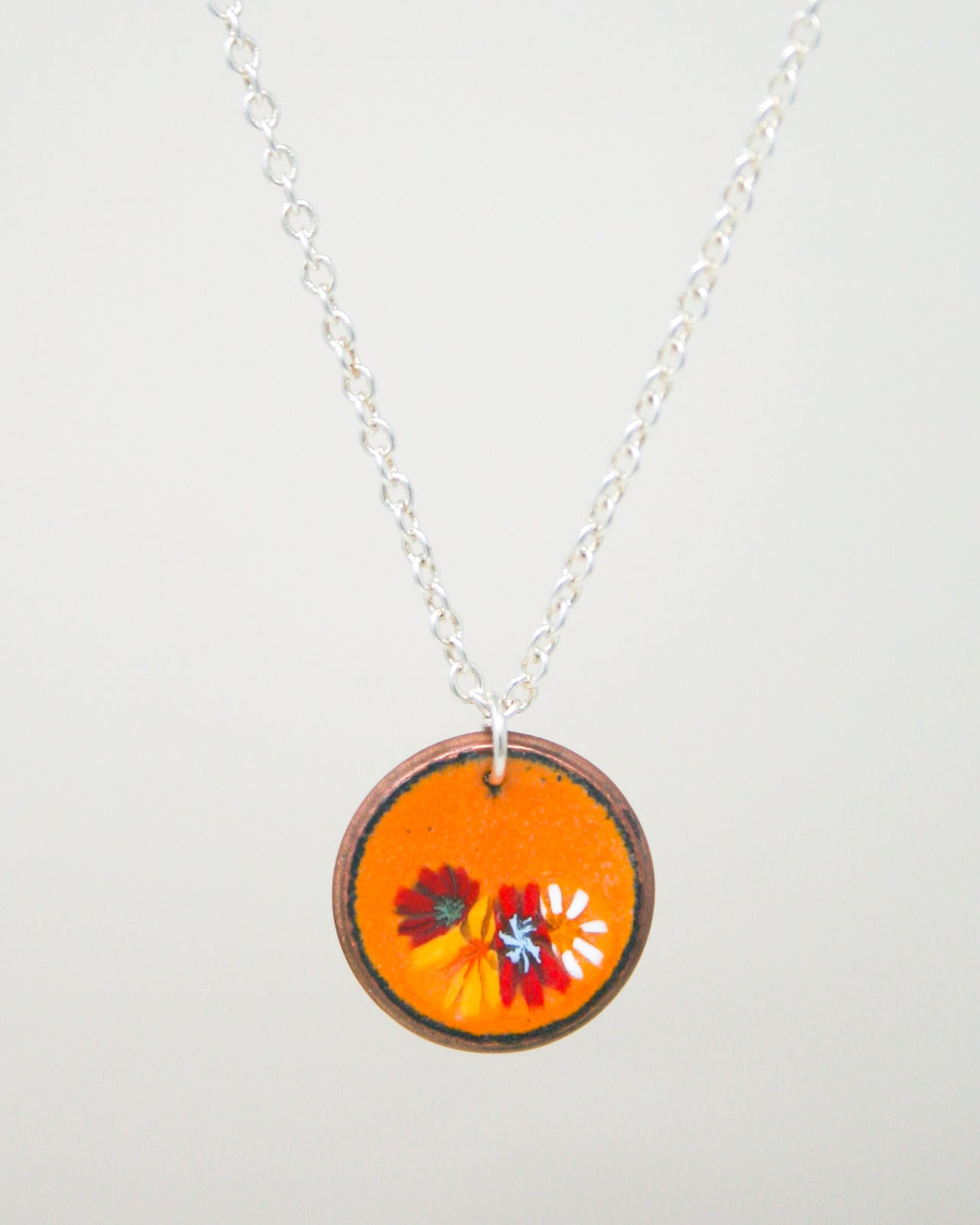 A necklace with a circular pendant featuring a vibrant floral design in shades of orange and red.