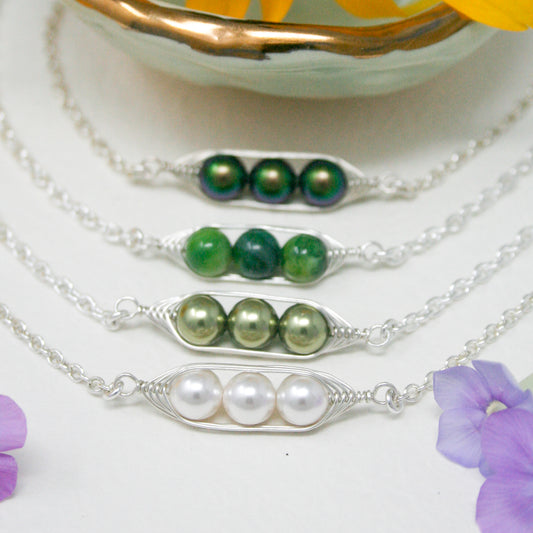 A collection of colorful necklaces with various colored beads, including white, green, and purple, arranged in a row on a white background.