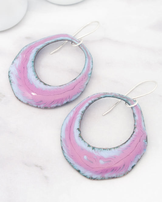 A pair of colorful earrings with a pink and blue color scheme, resting on a white marble surface.