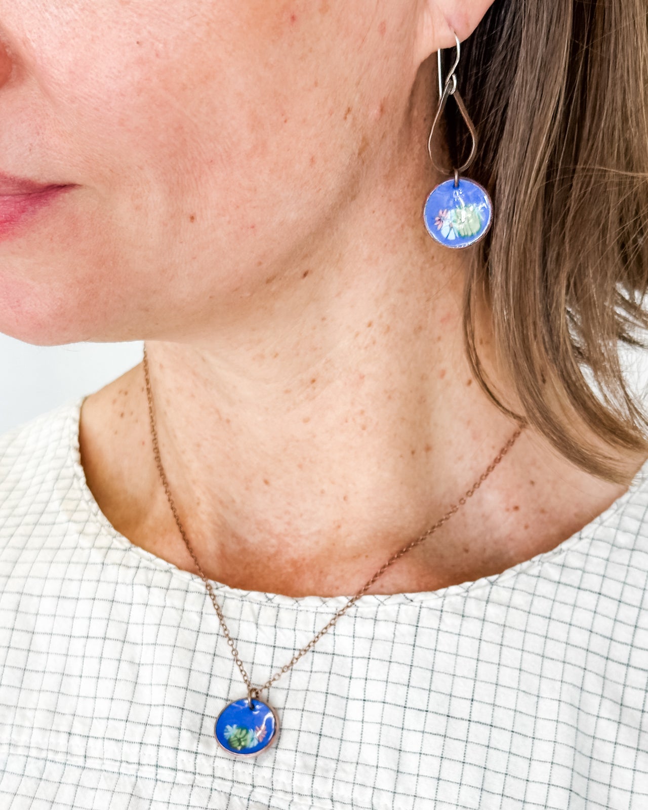 A woman wearing a necklace with a blue pendant and earrings with a blue design.