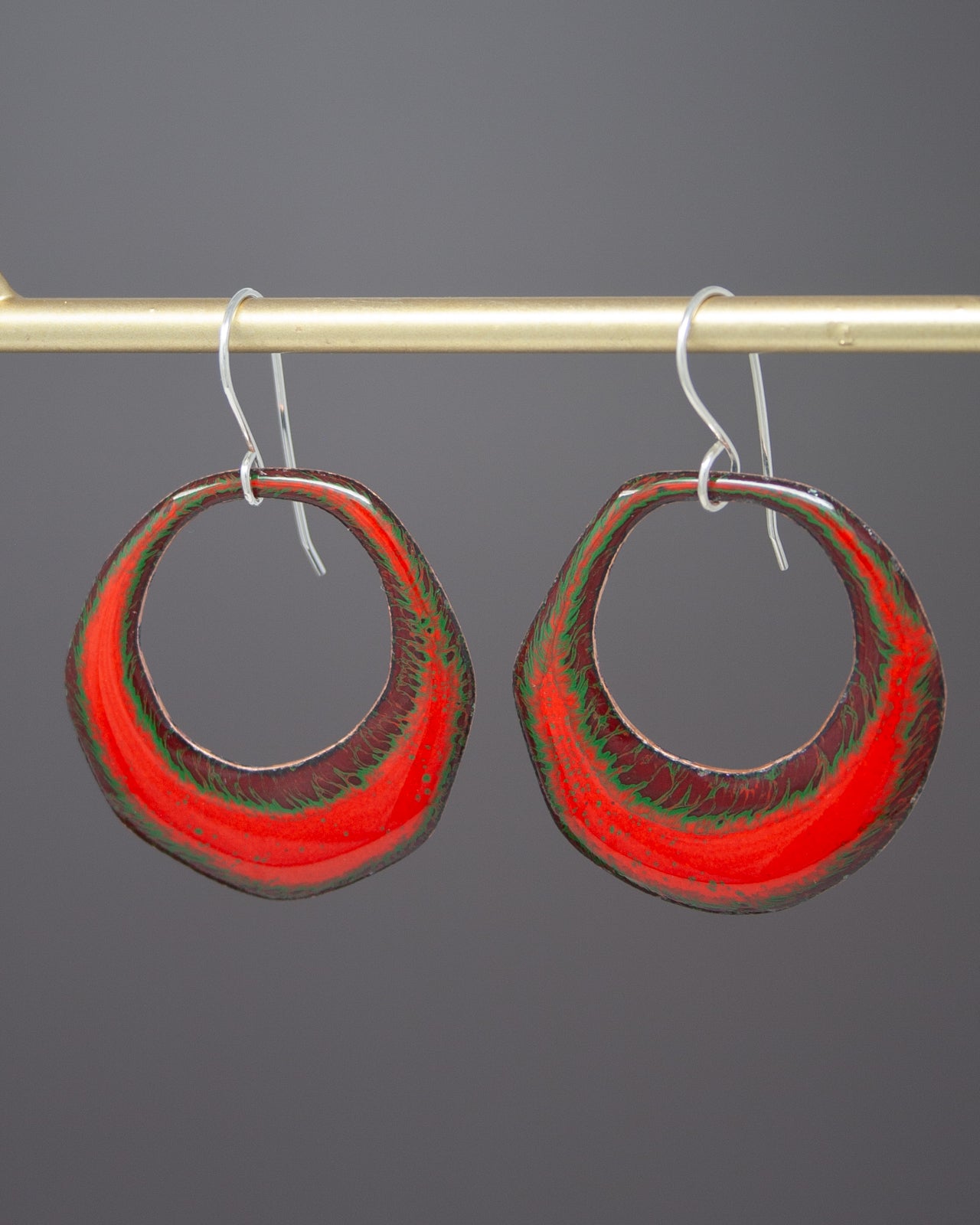 A pair of red and green hoop earrings hanging from a metal hook.