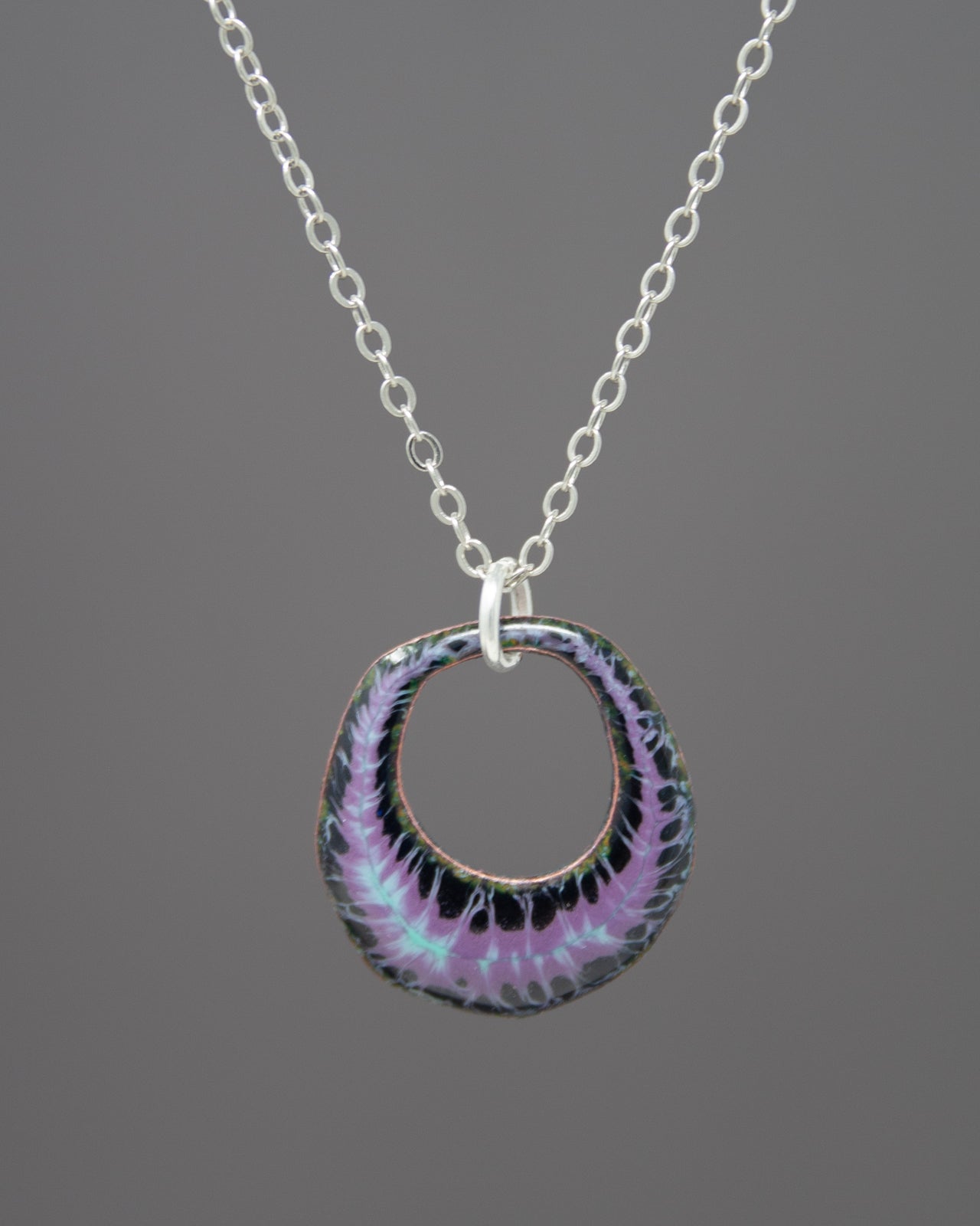 A silver necklace with a circular pendant featuring a purple and black tie-dye pattern.