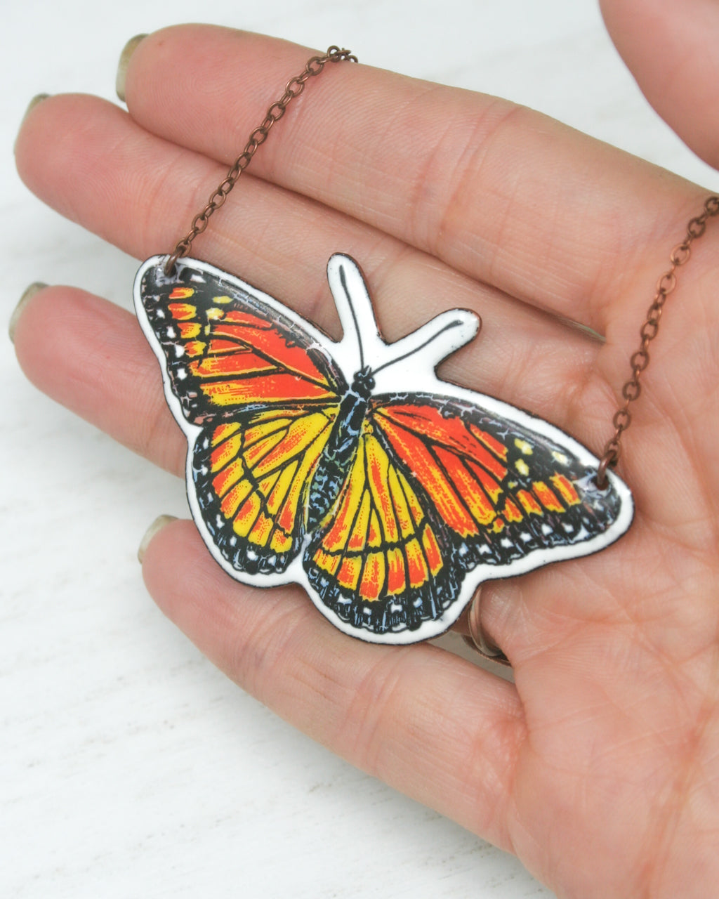a hand holding a small orange butterfly on a chain