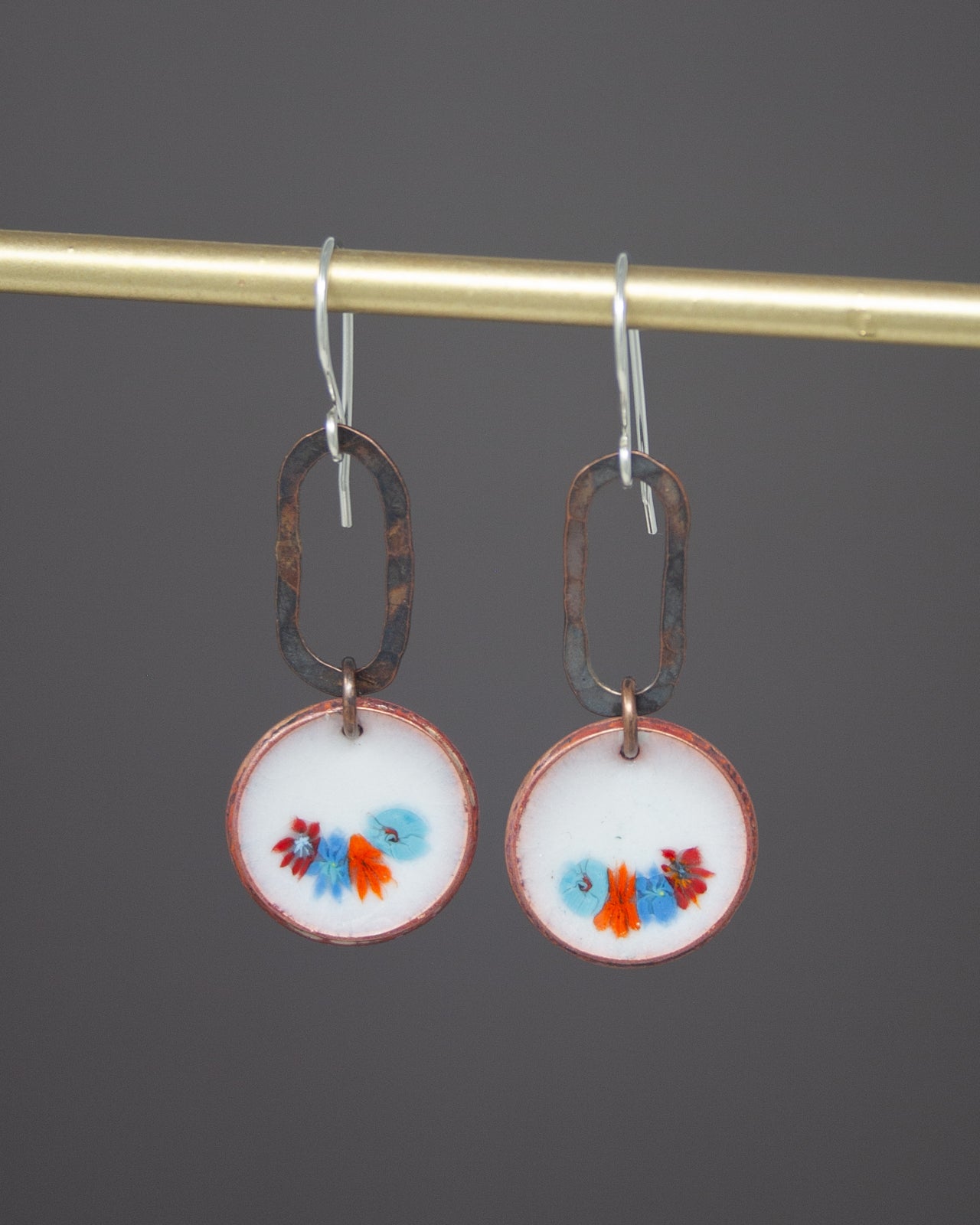 A pair of earrings with a floral design on the circular pendants, hanging from a gold-colored metal hook.