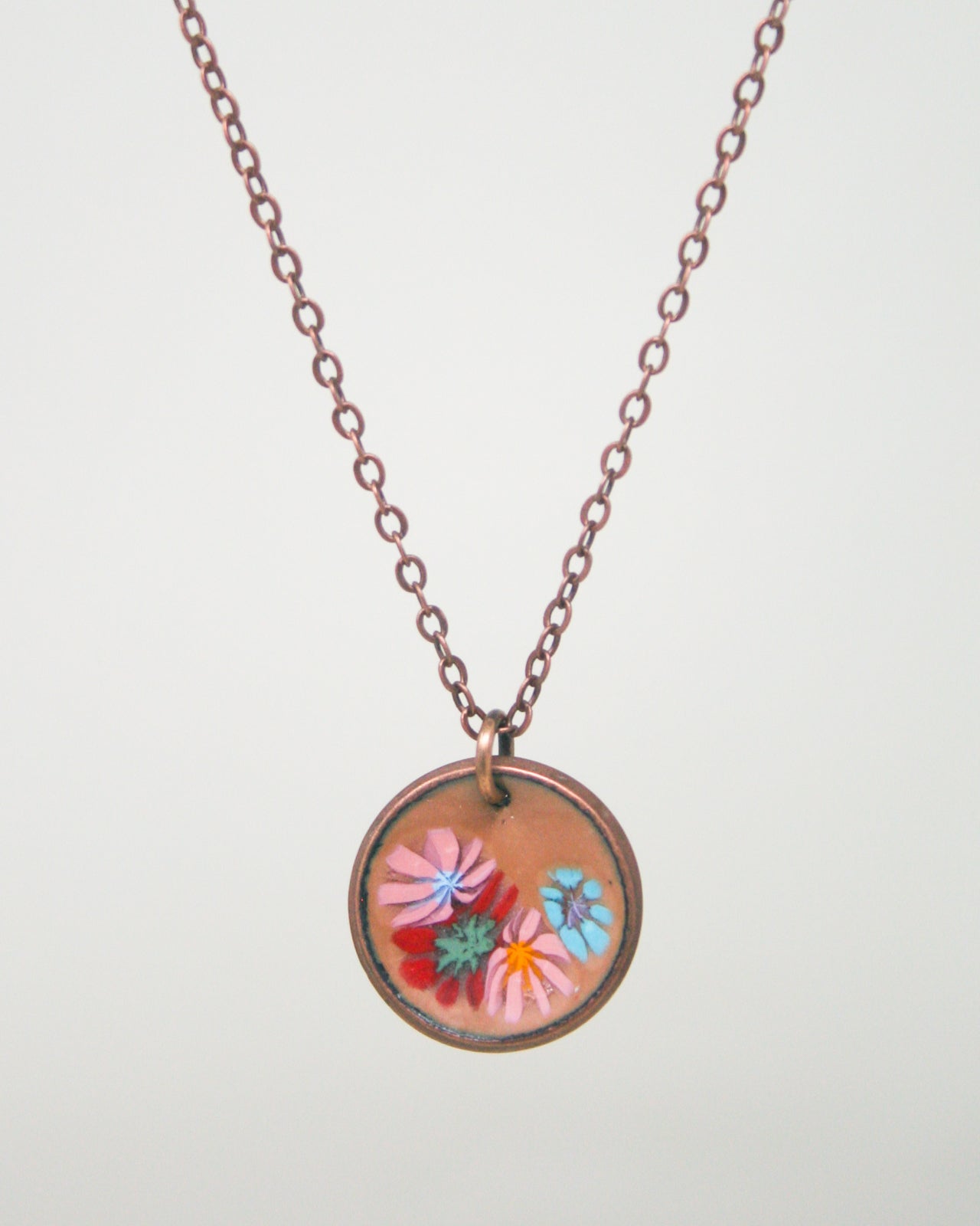 A round pendant necklace with a chain and a circular design featuring colorful flowers.