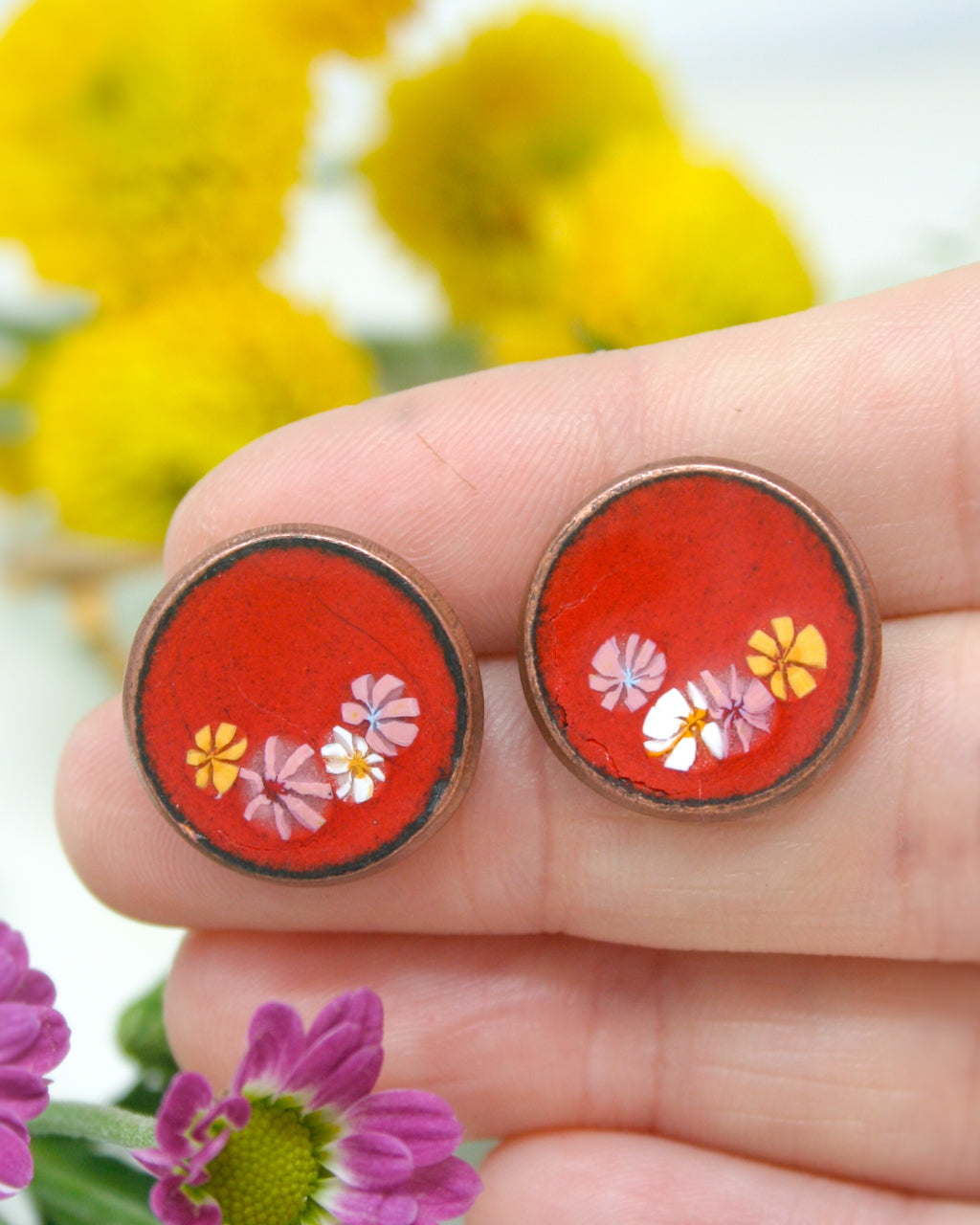 a hand holding a pair of earrings with flowers on them