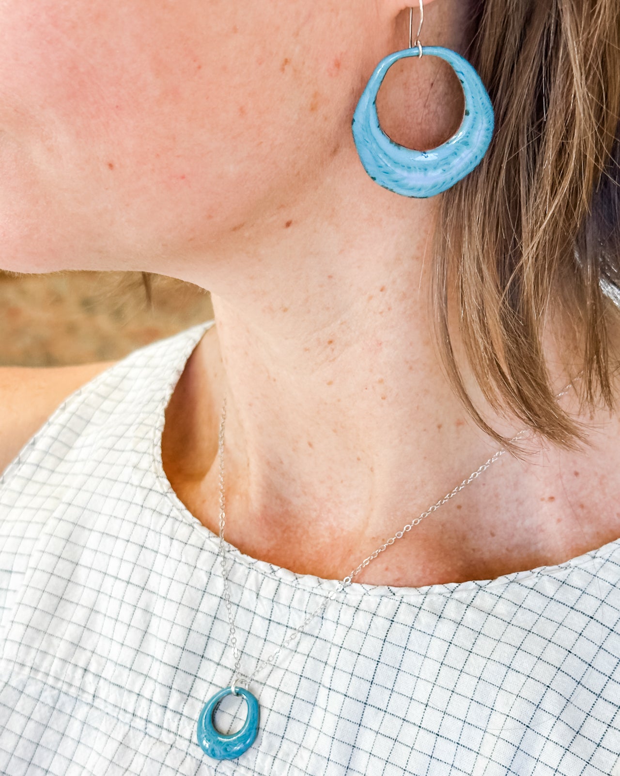A close-up view of a woman's neck and earrings, with a necklace and pendant visible.