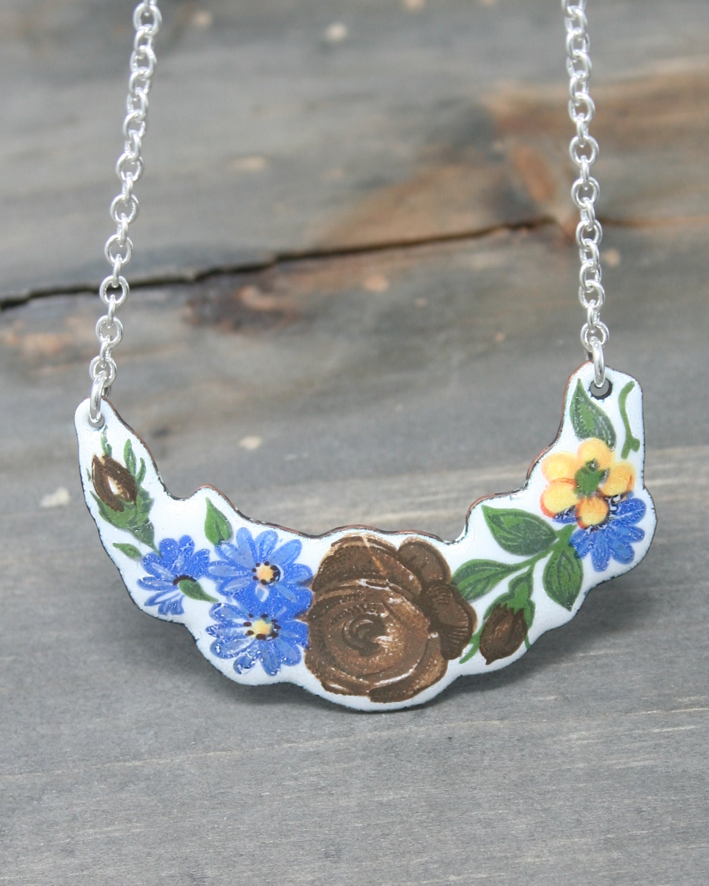 A necklace with a floral design, featuring blue and yellow flowers and a brown rose.