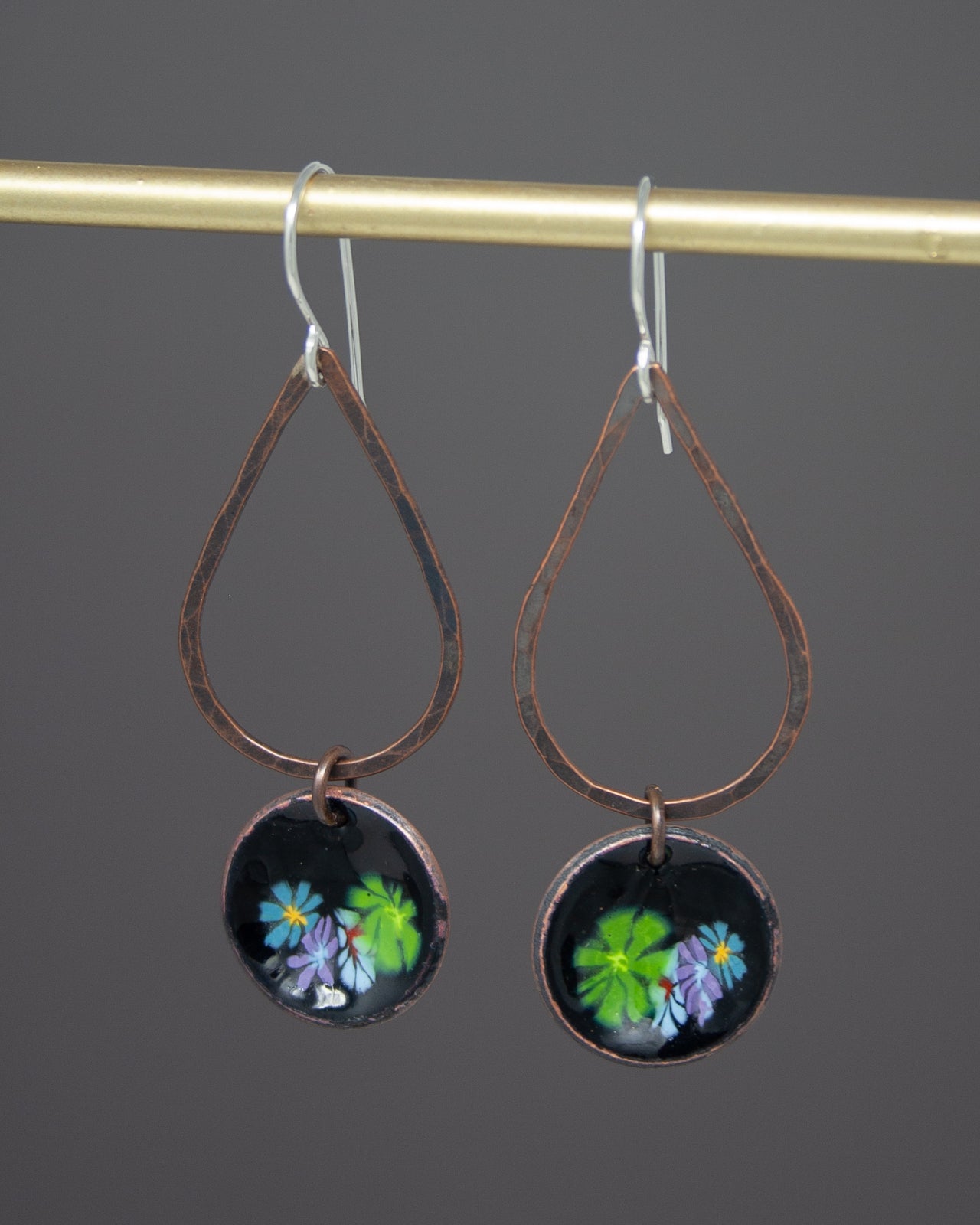 A pair of earrings with a floral design on the circular pendants hanging from a gold-colored metal hook.