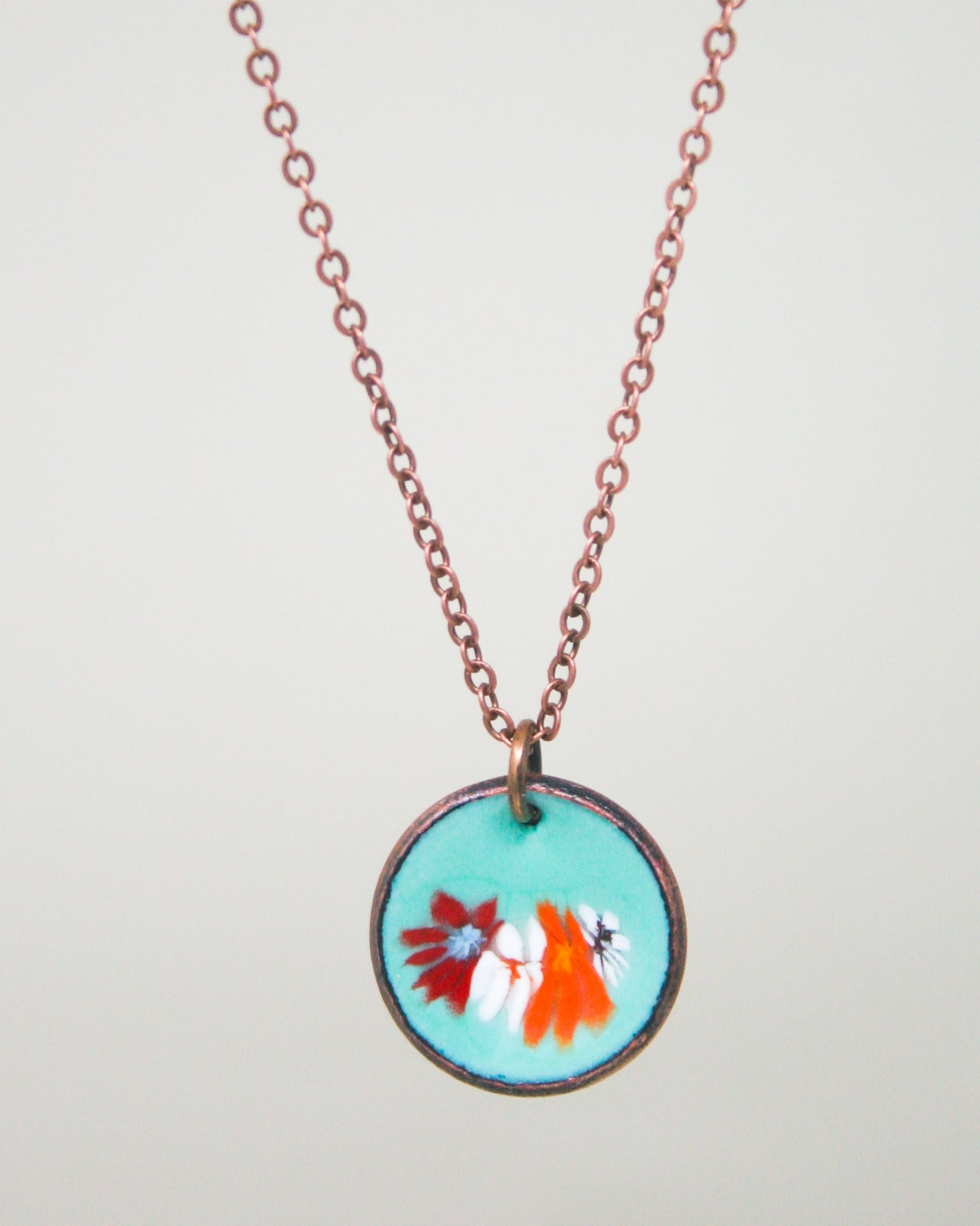 A necklace with a circular pendant featuring a floral design in turquoise and red colors.
