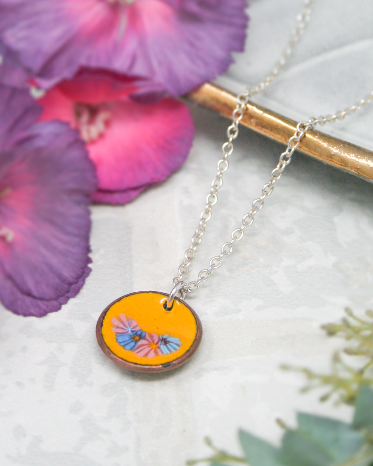 A necklace with a circular pendant featuring a floral design, surrounded by purple and pink flowers.