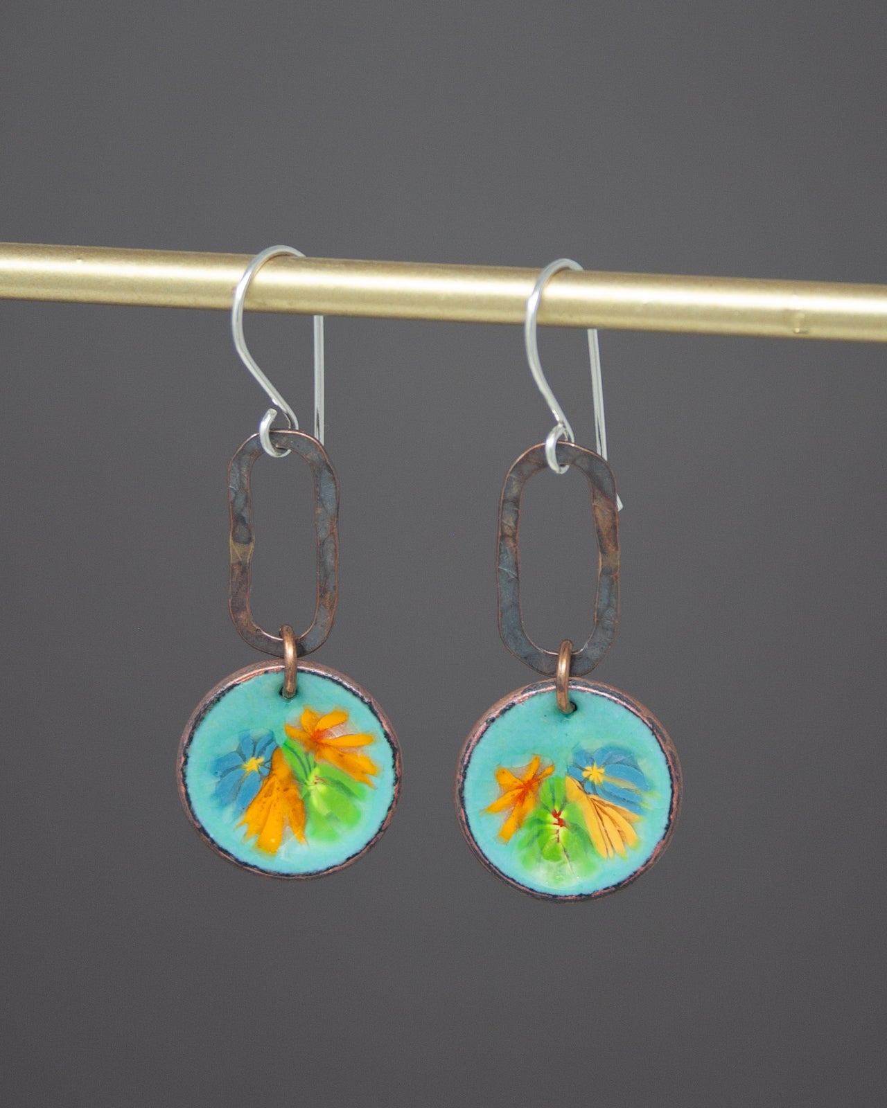 A pair of earrings with a floral design on the circular pendants, hanging from a gold-colored metal hook.