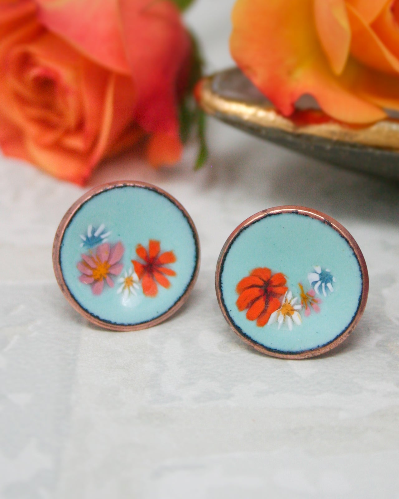 two round earrings with blue and orange floral designs, placed on a white surface.