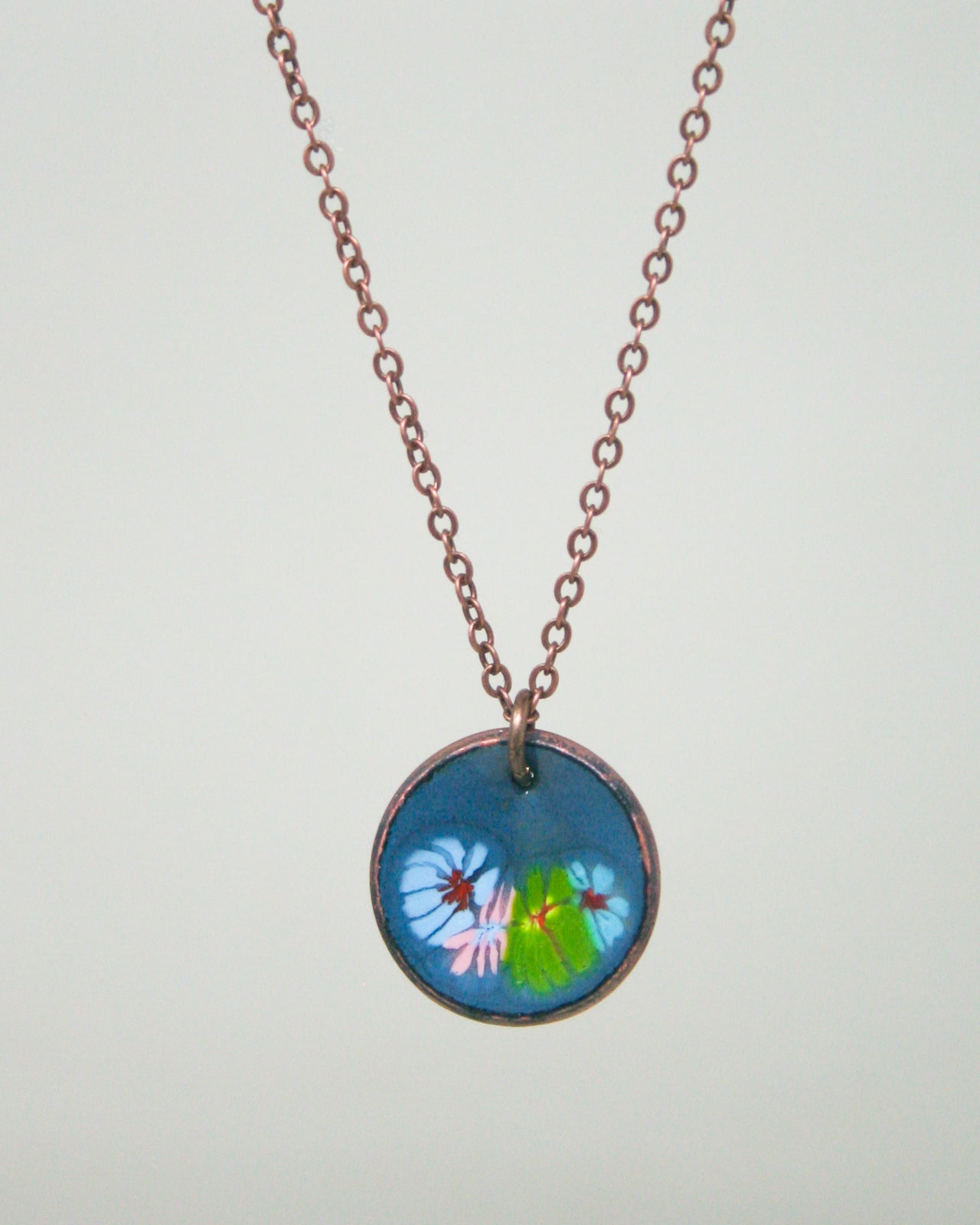 A necklace with a circular pendant featuring a floral design in blue, green, and pink colors.