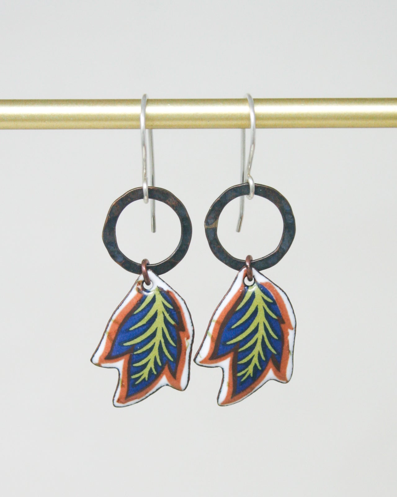 A pair of earrings with leaf-shaped designs hanging from a gold-colored metal bar.