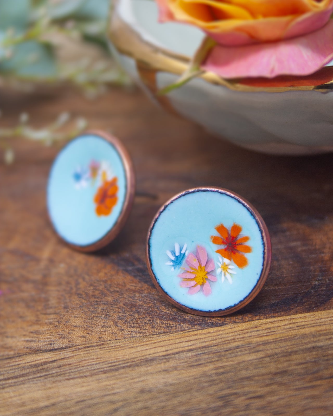two round earrings with blue and orange floral designs, placed on a wooden surface.