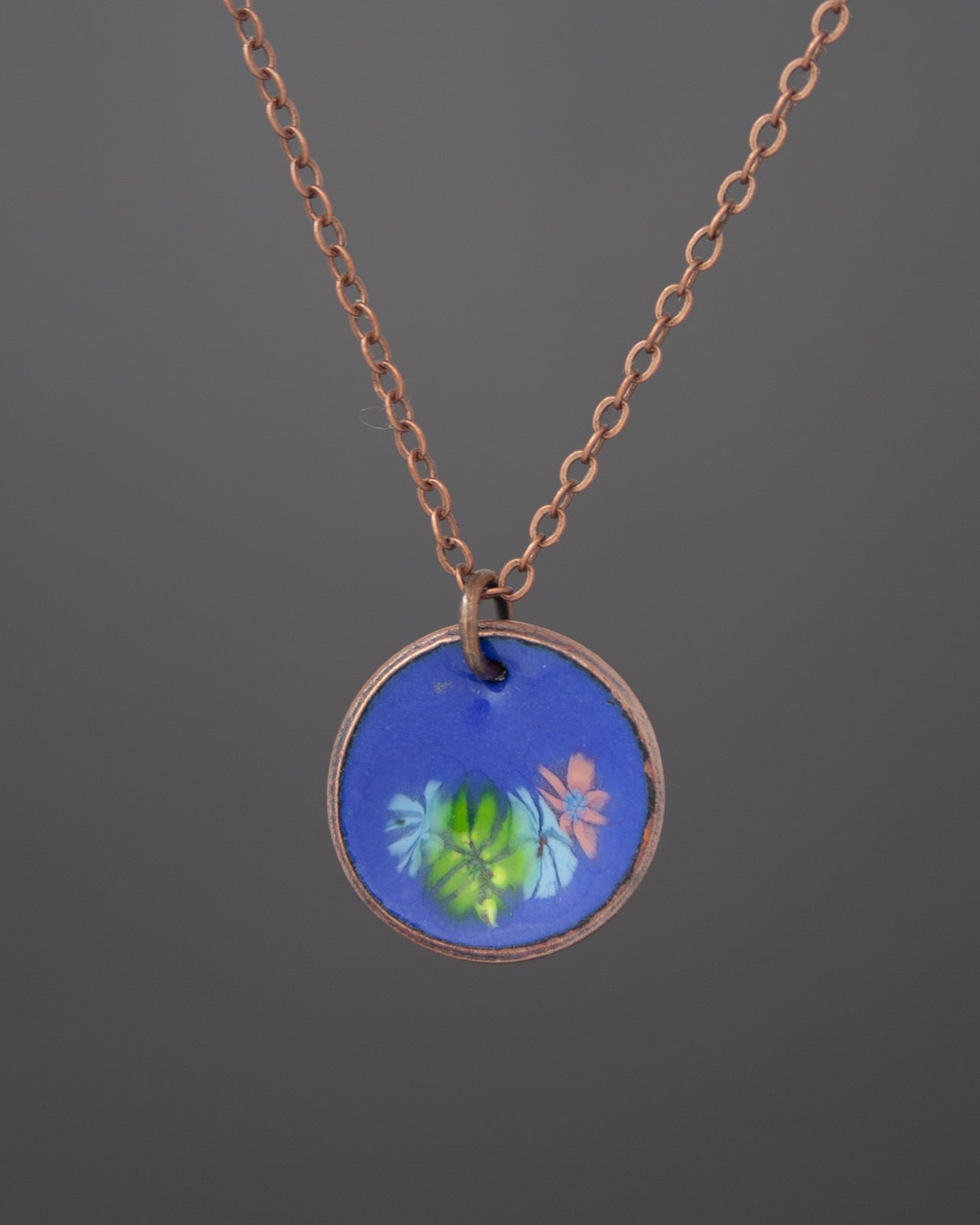 A necklace with a circular pendant featuring a floral design in blue and green colors.