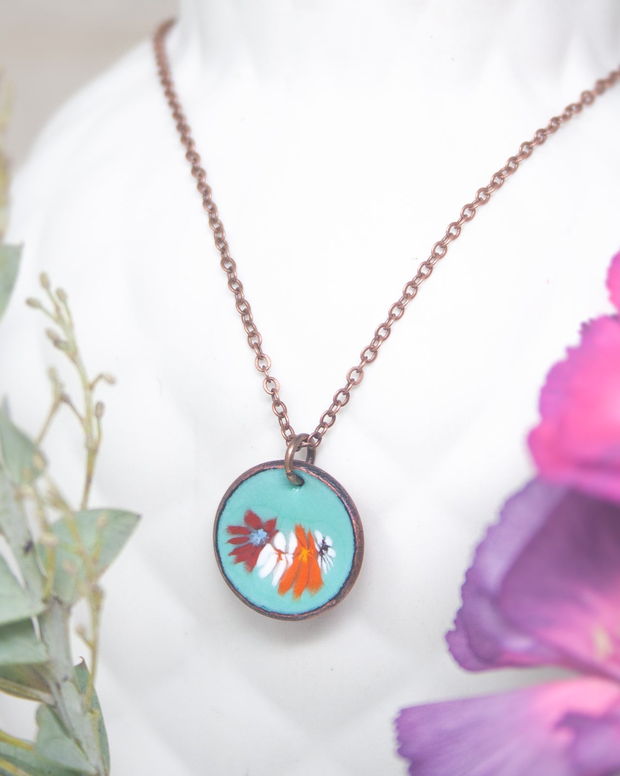 A necklace with a circular pendant featuring a floral design in turquoise and orange colors.