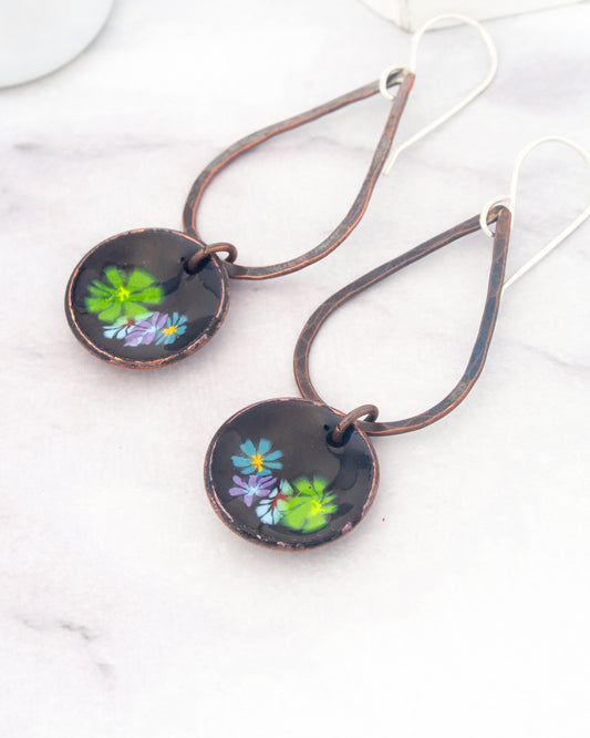 A pair of earrings with a floral design on the circular pendants, resting on a white marble surface.